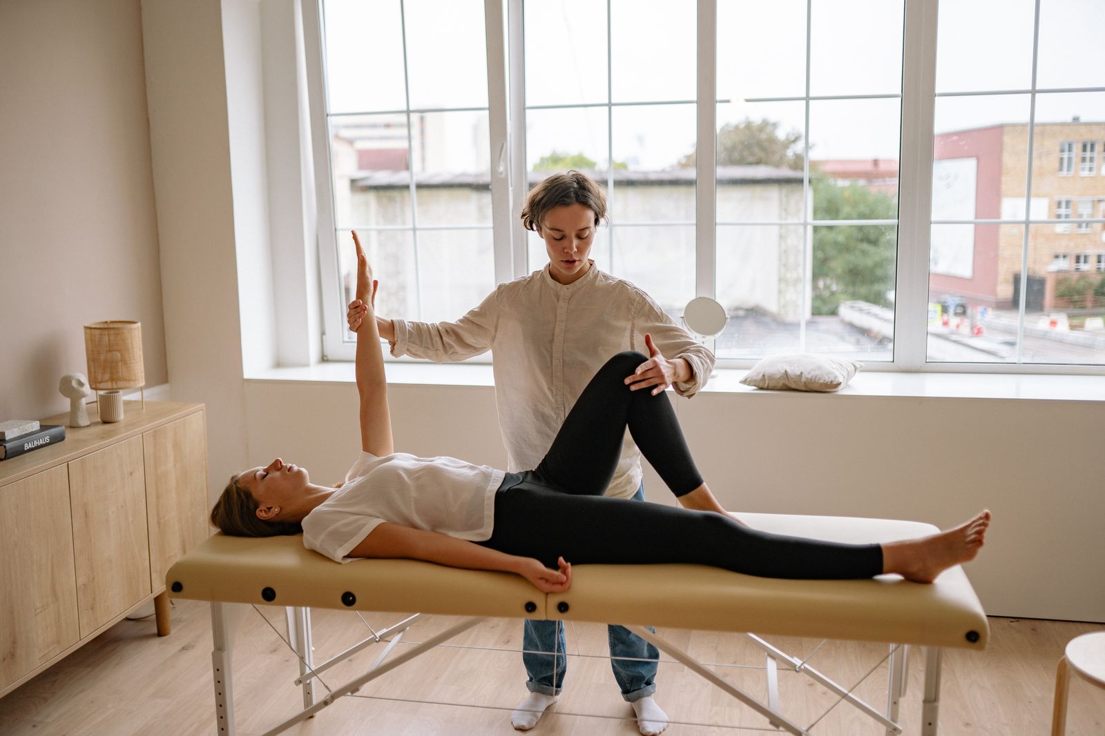 Therapist providing hands-on treatment to a woman lying on a treatment table in a bright clinic